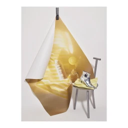 Glossier body cream and metallic silver boot on small grey stool beneath draped gold and white paper