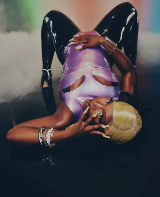 Woman in a lilac latex bodysuit strikes an inverted pose, showcasing a futuristic fashion style with sleek and shiny textures against a smoky background.