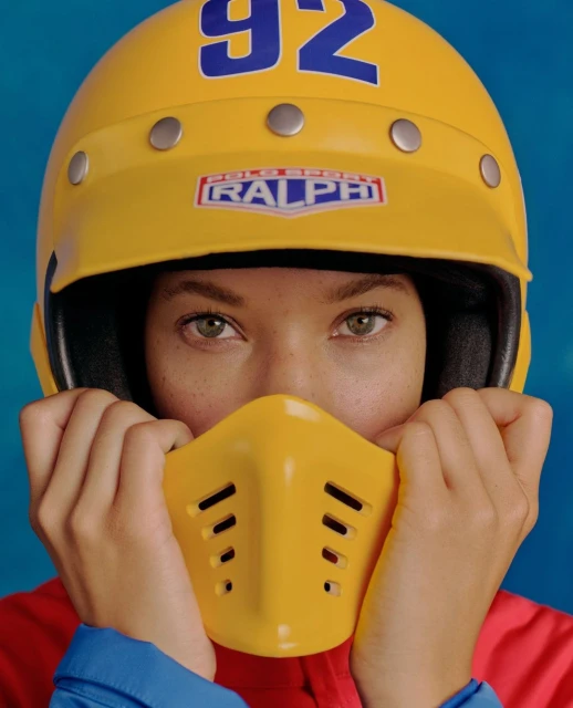 Close-up of a person wearing a yellow helmet and face guard, with the number 92 and the brand logo 'Polo Sport Ralph' visible.