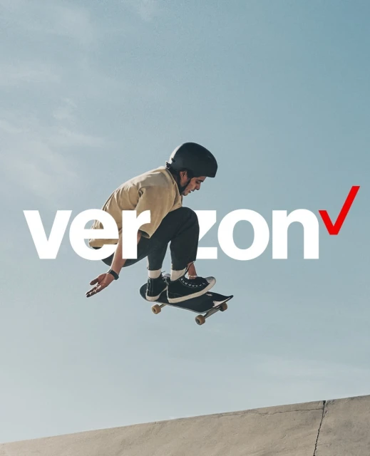 A young adult man in mid-air on a skateboard, wearing a helmet and casual clothes, against a bright sky with the Verizon logo.