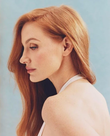 Profile portrait of a fair-skinned woman with long red hair wearing a white top against a light blue background.