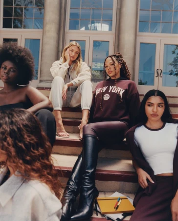 Group of five diverse young women in stylish maroon and white clothing sit on outdoor building steps in an eye-level portrait.