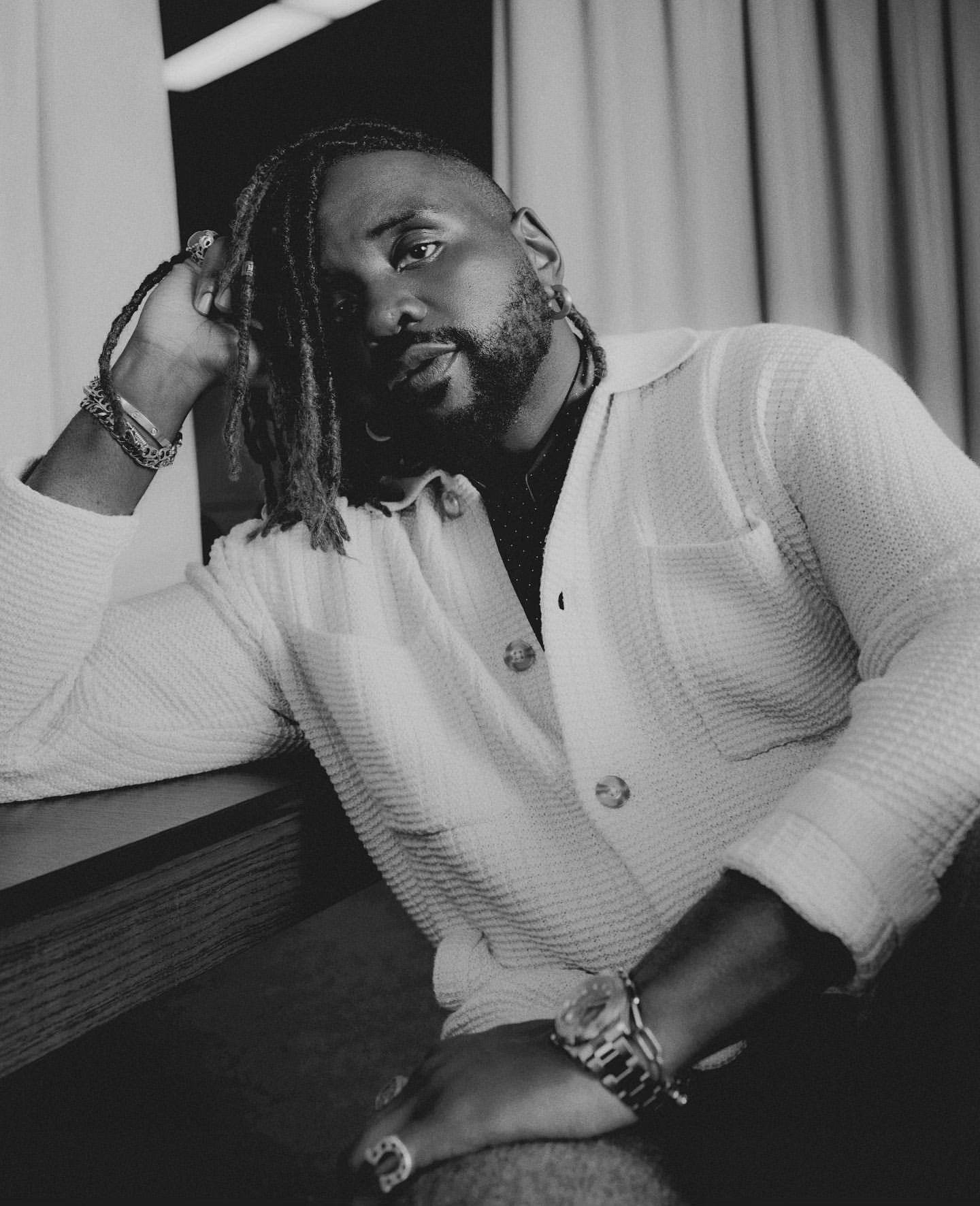Black man with dreadlocks wearing a textured knit cardigan and silver bracelets, photographed in black and white by Micaiah Carter.