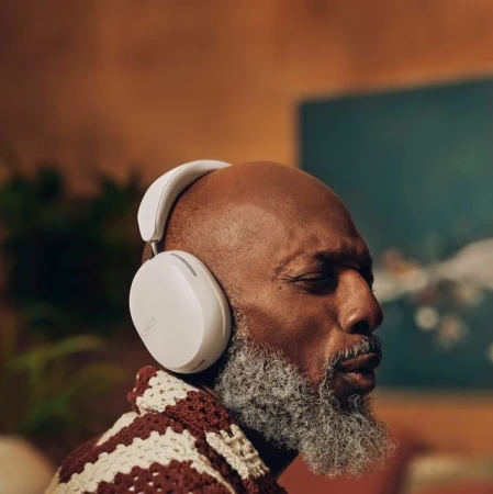 Mature African-American man with closed eyes wearing white headphones and a brown crocheted sweater in a softly lit indoor setting.