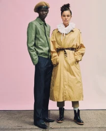 Two fashion models posing against a pink gradient backdrop, a man in a green jacket and a woman in a tan trench coat.