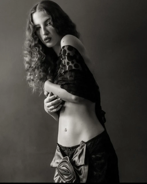 Monochrome portrait of a woman with long curly hair, wearing black lace lingerie and a polka dot shawl, against a dark background.