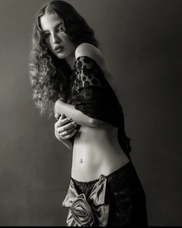 Monochrome portrait of a woman with long curly hair, wearing black lace lingerie and a polka dot shawl, against a dark background.