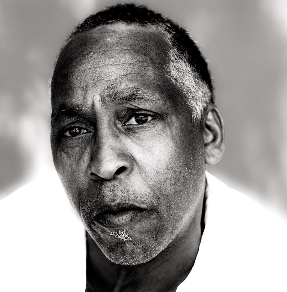 Black and white close-up portrait of an adult Black male with a serious facial expression, shot in a photo studio setting.