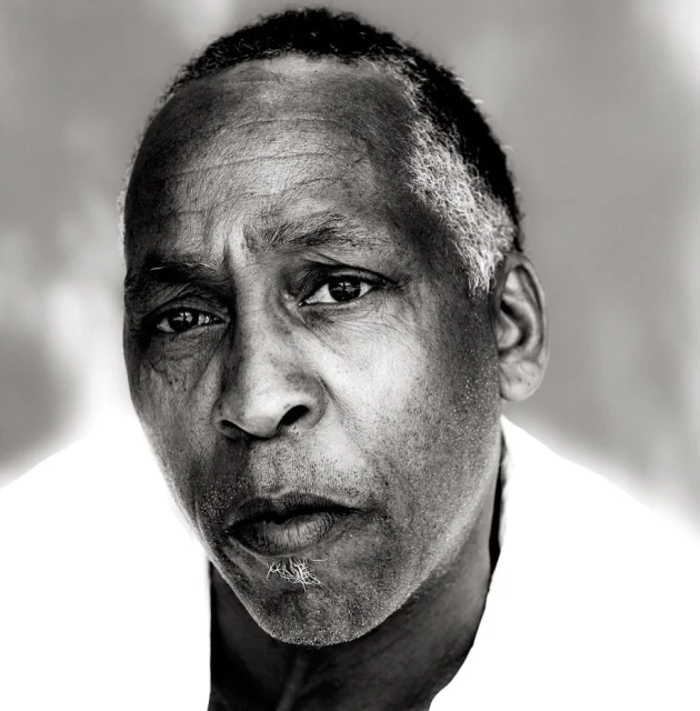 Black and white close-up portrait of an adult Black male with a serious facial expression, shot in a photo studio setting.