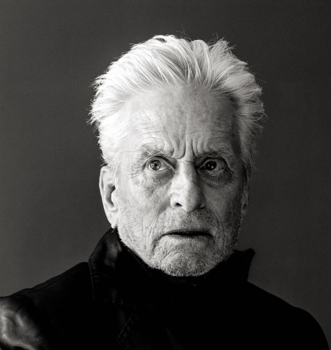 Black and white portrait of an elderly adult male with gray hair wearing a dark turtleneck sweater against a grey background.