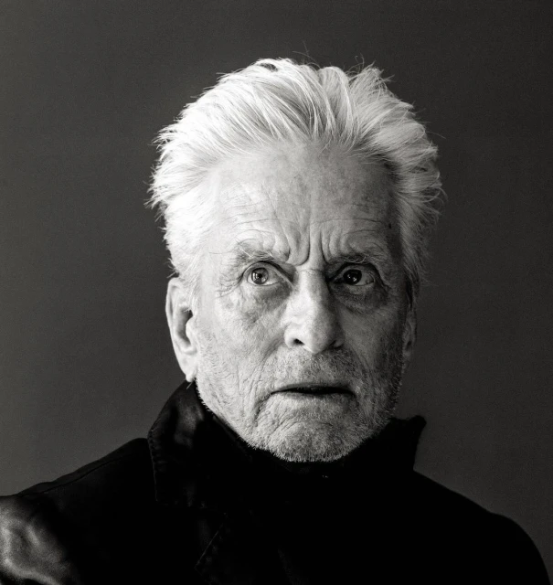 Black and white portrait of an elderly adult male with gray hair wearing a dark turtleneck sweater against a grey background.