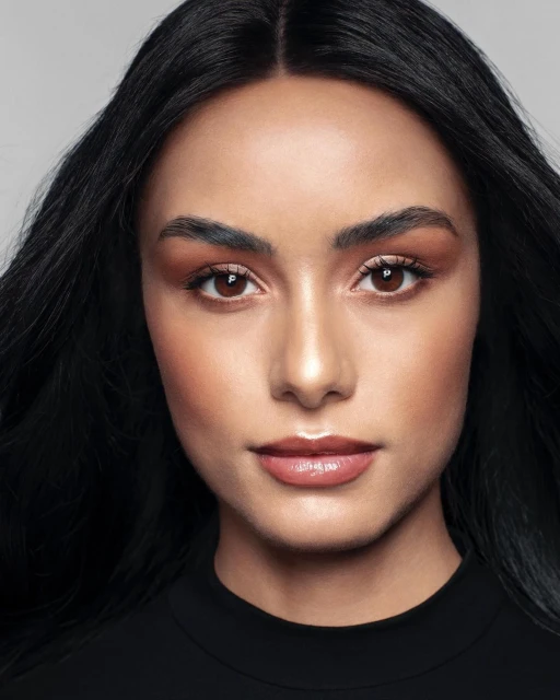 Close-up portrait of a brunette woman with neutral makeup and a black top against a grey backdrop, professionally lit in a studio.