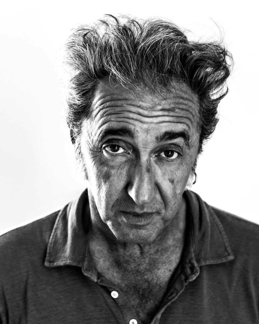 Monochrome close-up portrait of an adult man with tousled hair wearing a collared shirt against a white background in eye-level shot.