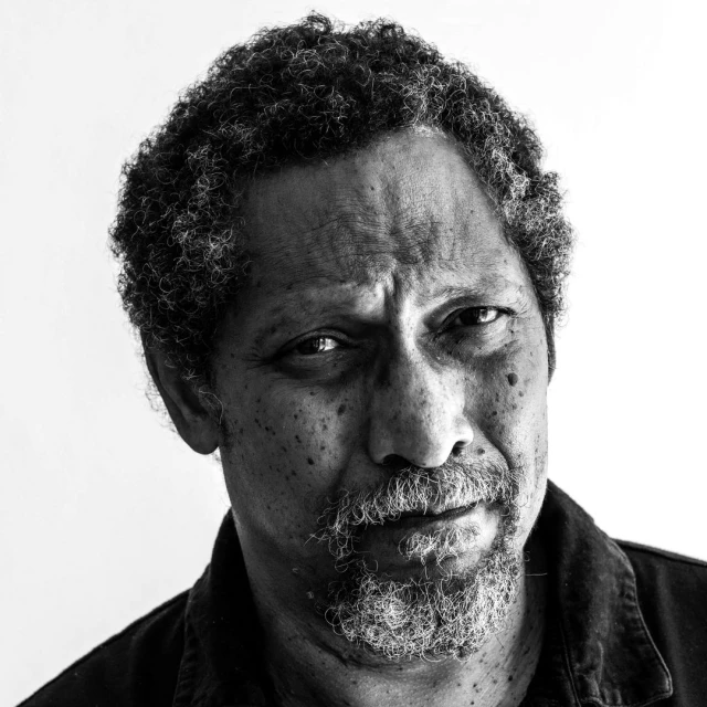 Monochrome portrait of an adult male with curly hair and a short beard against a white backdrop, close-up shot.