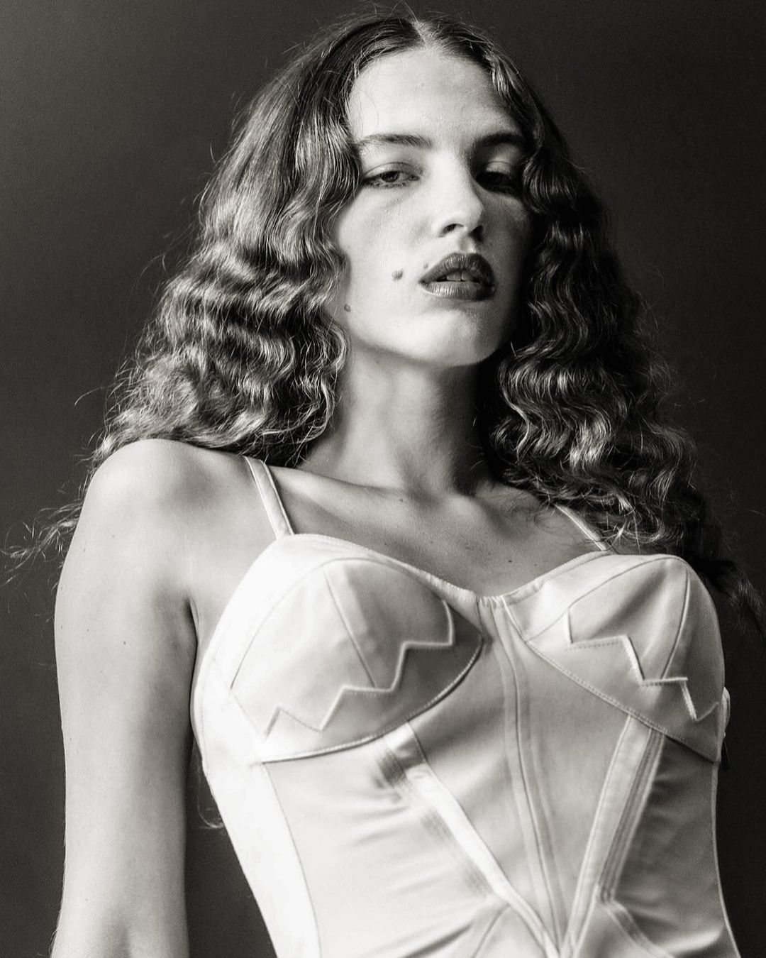 Portrait of a woman with long wavy hair wearing a white corset top, photographed by Michael Avedon.