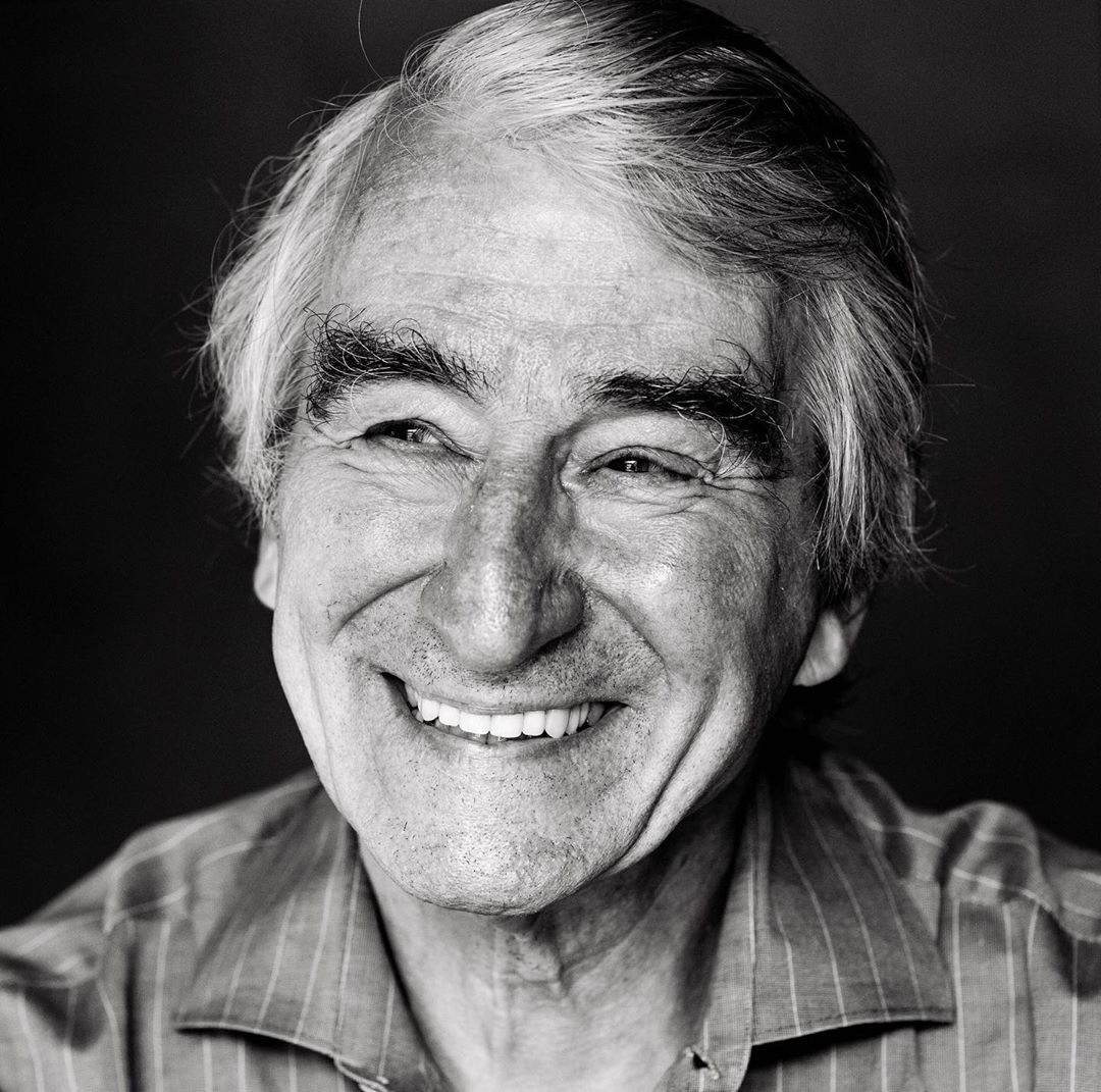 Black and white portrait of an elderly adult male with graying hair, smiling and wearing a striped collared shirt.