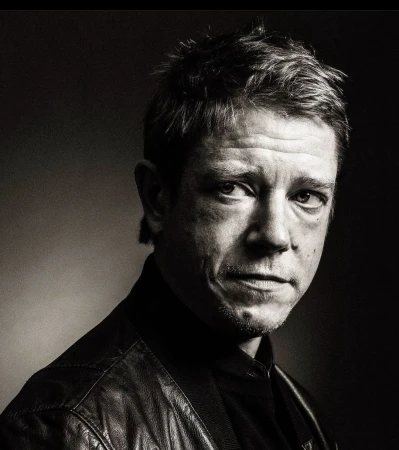 Monochrome portrait of a man in his 40s wearing a dark leather jacket against a dark background