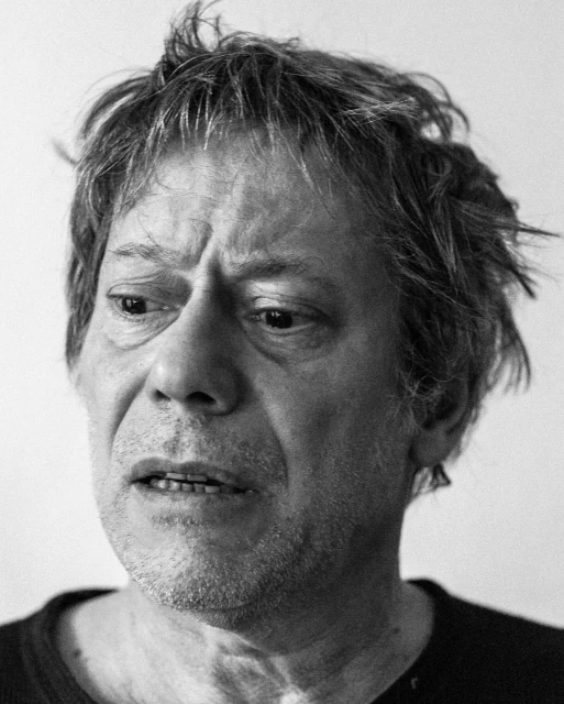 Black and white portrait of a mature adult male looking down and away from the camera with a neutral expression and slightly disheveled hair.