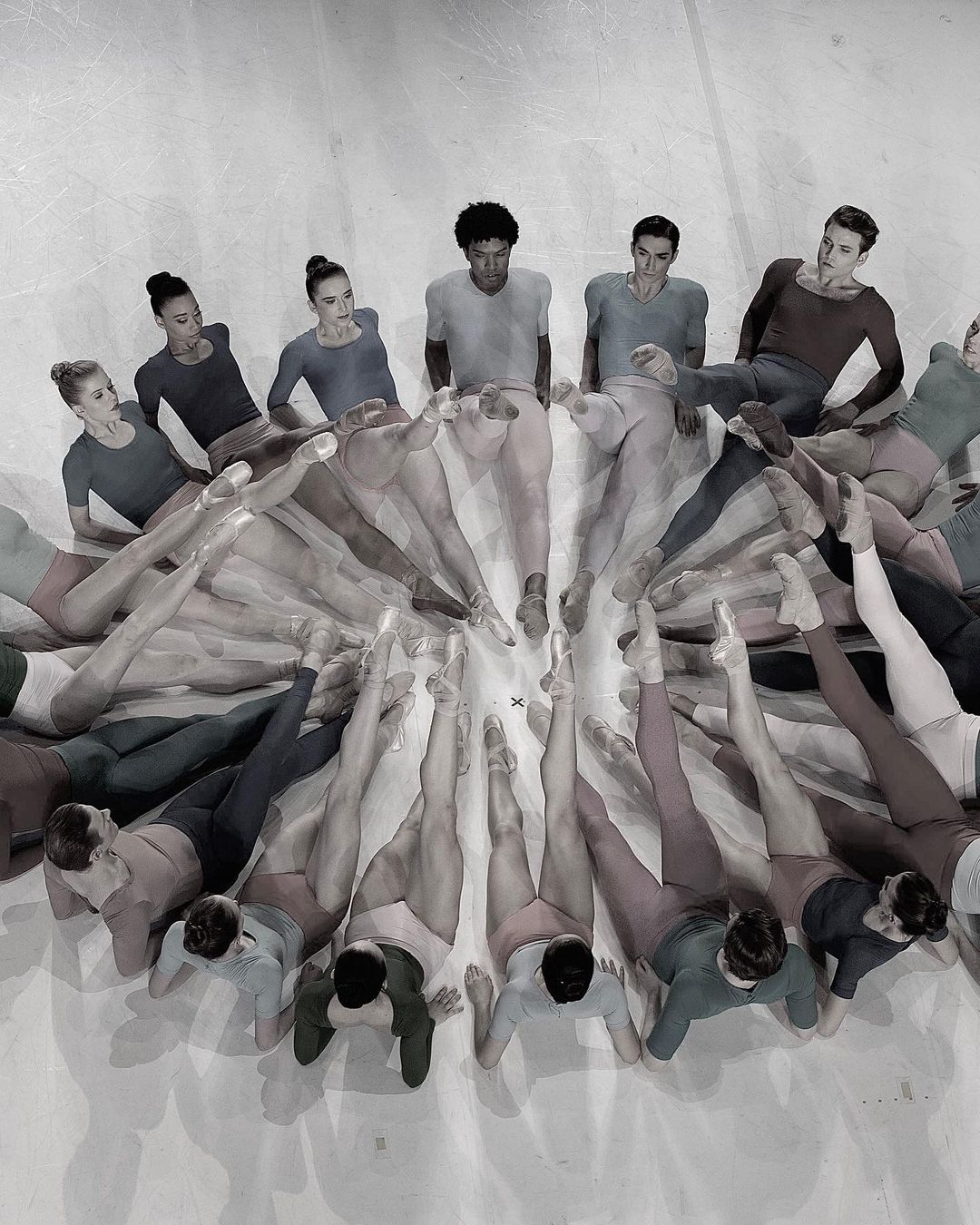 Overhead shot of dancers in leotards and tights arranged in a radial pattern, showcasing their legs and feet, set against a light backdrop.
