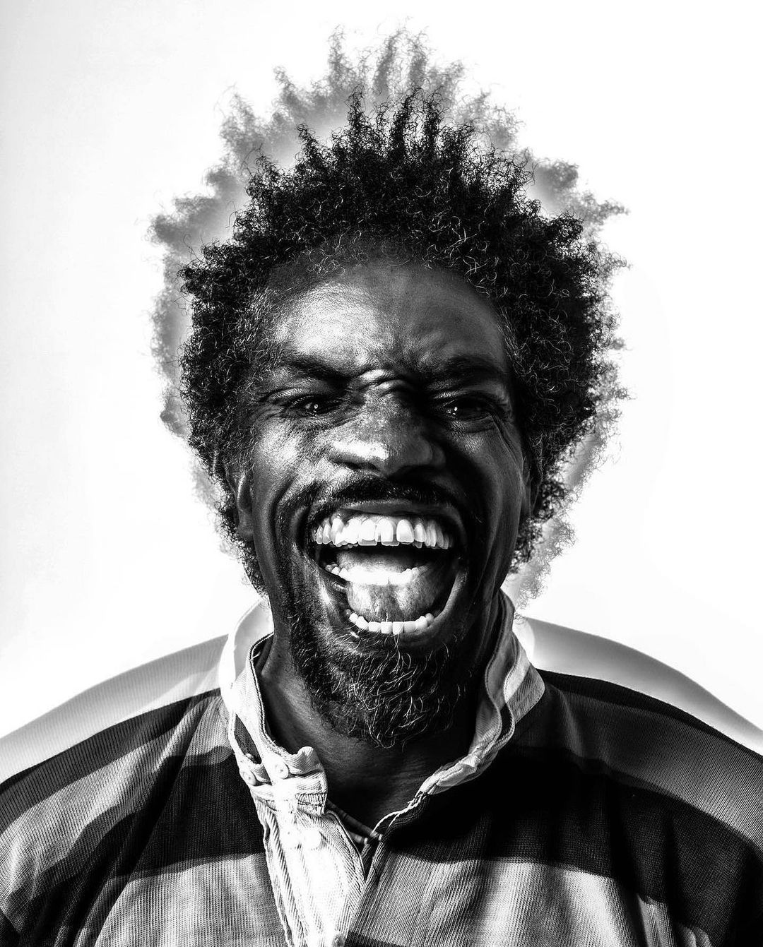 Black and white portrait of an African American man with an afro, grinning widely and wearing a striped shirt against a white background.
