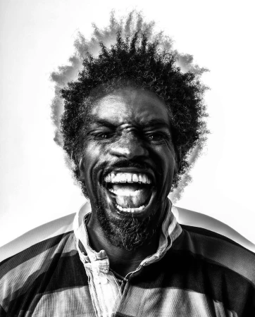 Black and white portrait of an African American man with an afro, grinning widely and wearing a striped shirt against a white background.