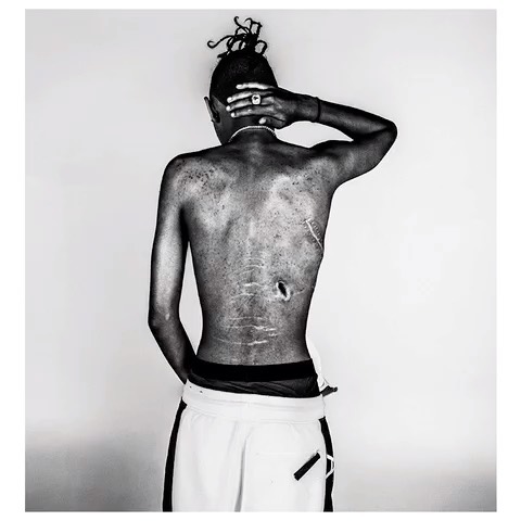 Striking black and white studio portrait featuring an adult male with a unique hairstyle, showcasing his bare back against a plain backdrop.