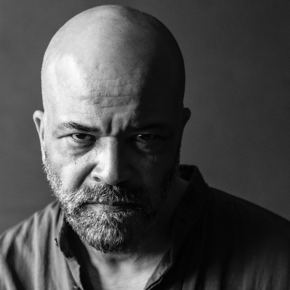 Black and white portrait of a bald adult man with a beard, looking directly at the camera with a serious expression.