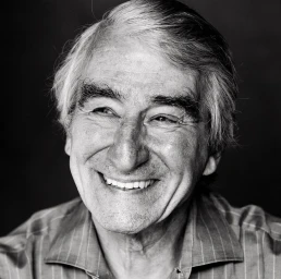 Close-up monochrome portrait of an elderly man smiling warmly against a dark background, photographed by Michael Avedon.