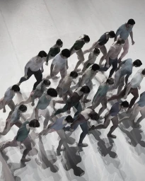 High-angle view of a large group of dancers in leotards moving across a plain light studio floor casting strong shadows