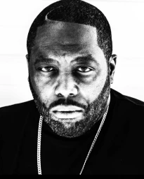 Close-up black and white portrait of a Black man wearing a dark t-shirt and a silver chain necklace.