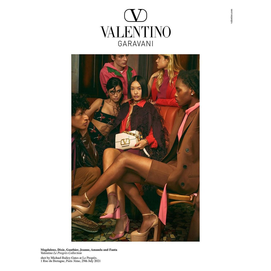 Valentino ad features a diverse group seated indoors; an Asian model holds a Valentino handbag, showcasing luxury fashion and accessories.