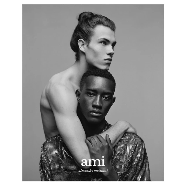 Black and white portrait of two adult males in a close embrace. One man wears a shimmering shirt and the other is shirtless.