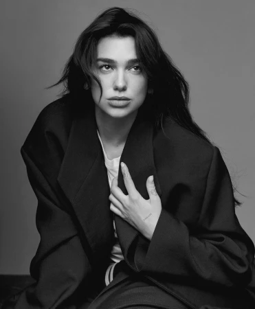 Monochrome portrait of Dua Lipa wearing an oversized dark blazer and white t-shirt against a grey background