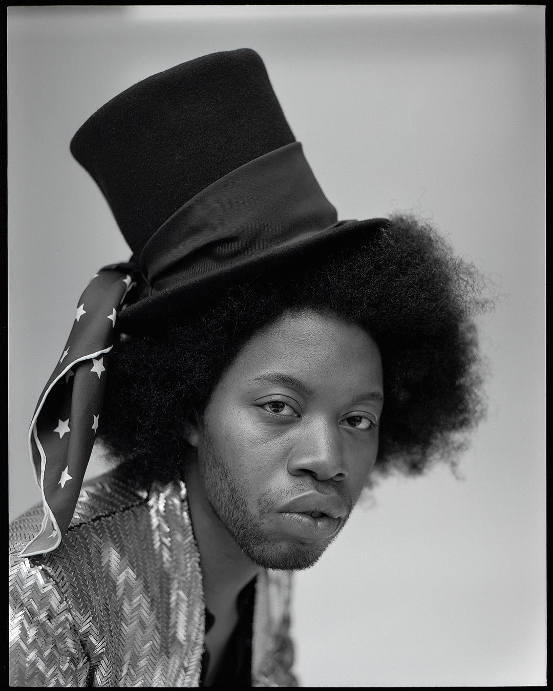 Portrait of an African American man with an afro wearing a sequined jacket and top hat with star scarf in a photo studio.