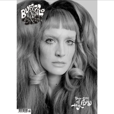 Black and white magazine cover featuring a woman with long, wavy hair, bold eye makeup, and a peace symbol hair clip.