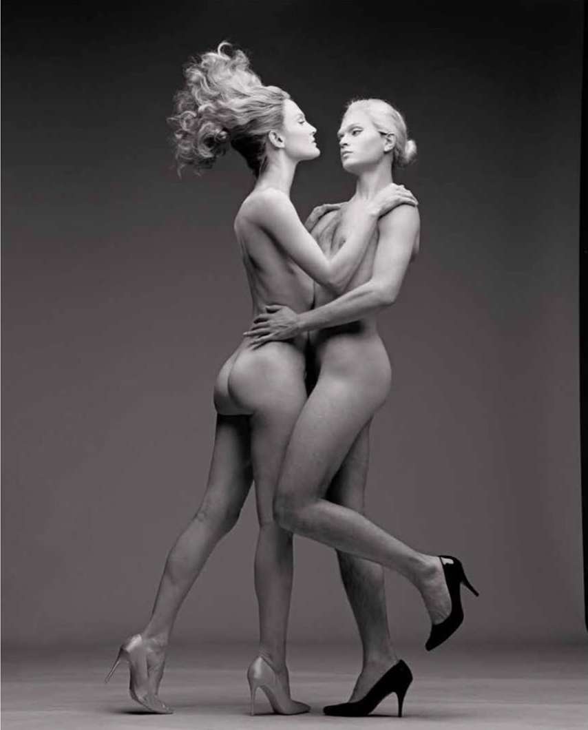 Striking black-and-white studio shot features two nude adult female fashion models with high heels in a unique embracing pose.