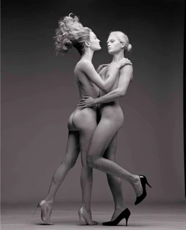 Striking black-and-white studio shot features two nude adult female fashion models with high heels in a unique embracing pose.