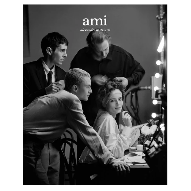 Black and white portrait of four people around a vanity mirror, including two young adults, an older woman having her hair styled.