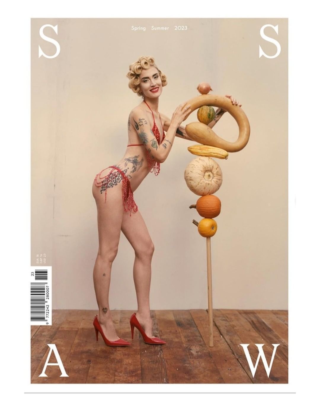 Magazine cover features a woman in a bikini posing with a stack of various gourds, set against a neutral backdrop, with red heels.