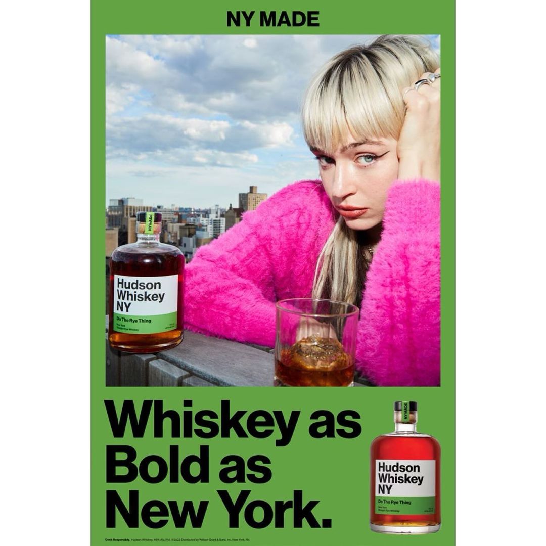 Advertisement featuring a woman in a pink sweater with blonde hair next to a bottle of Hudson Whiskey and a glass of whiskey.