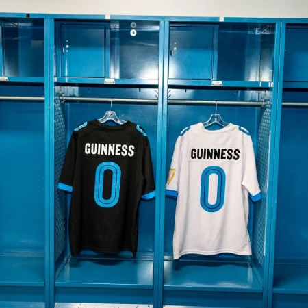 Two Guinness-branded jerseys, one black and one white, hang in adjacent blue metal lockers, presenting a clean and symmetrical locker room scene.