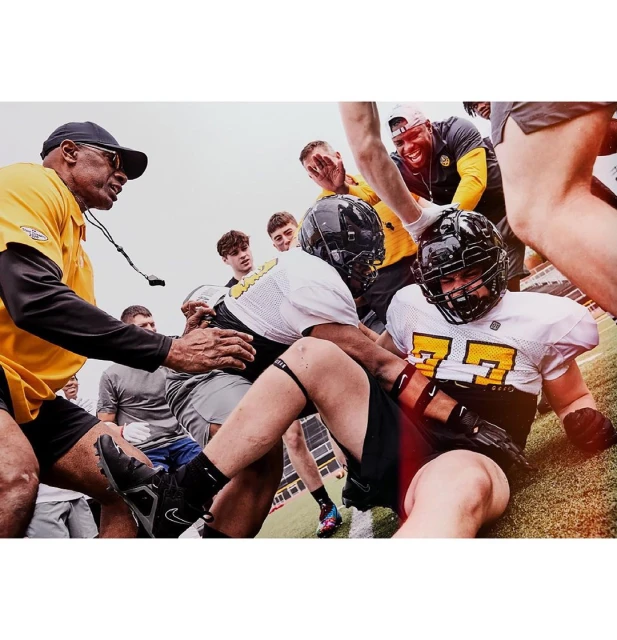 American football players and coach in uniform on the field during the game, black and yellow uniform, group of people cheering.