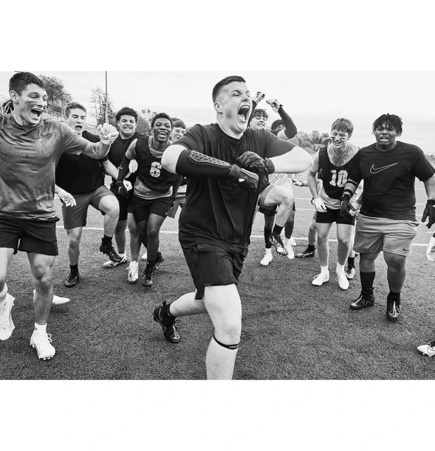 Monochrome action shot of a group of young male athletes celebrating a victory on a sports field with expressive excitement and energy.