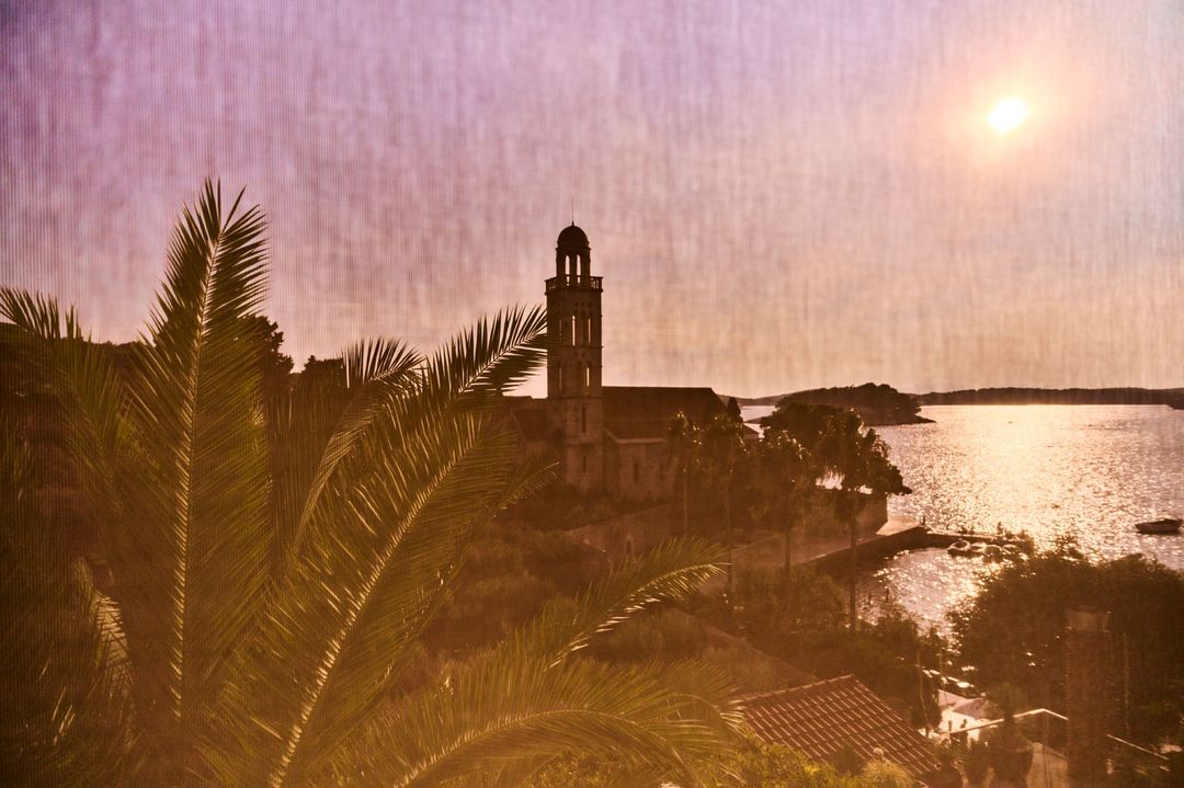 Coastal view featuring a church tower and palm trees, capturing a serene landscape with a mix of architecture and nature in soft light.