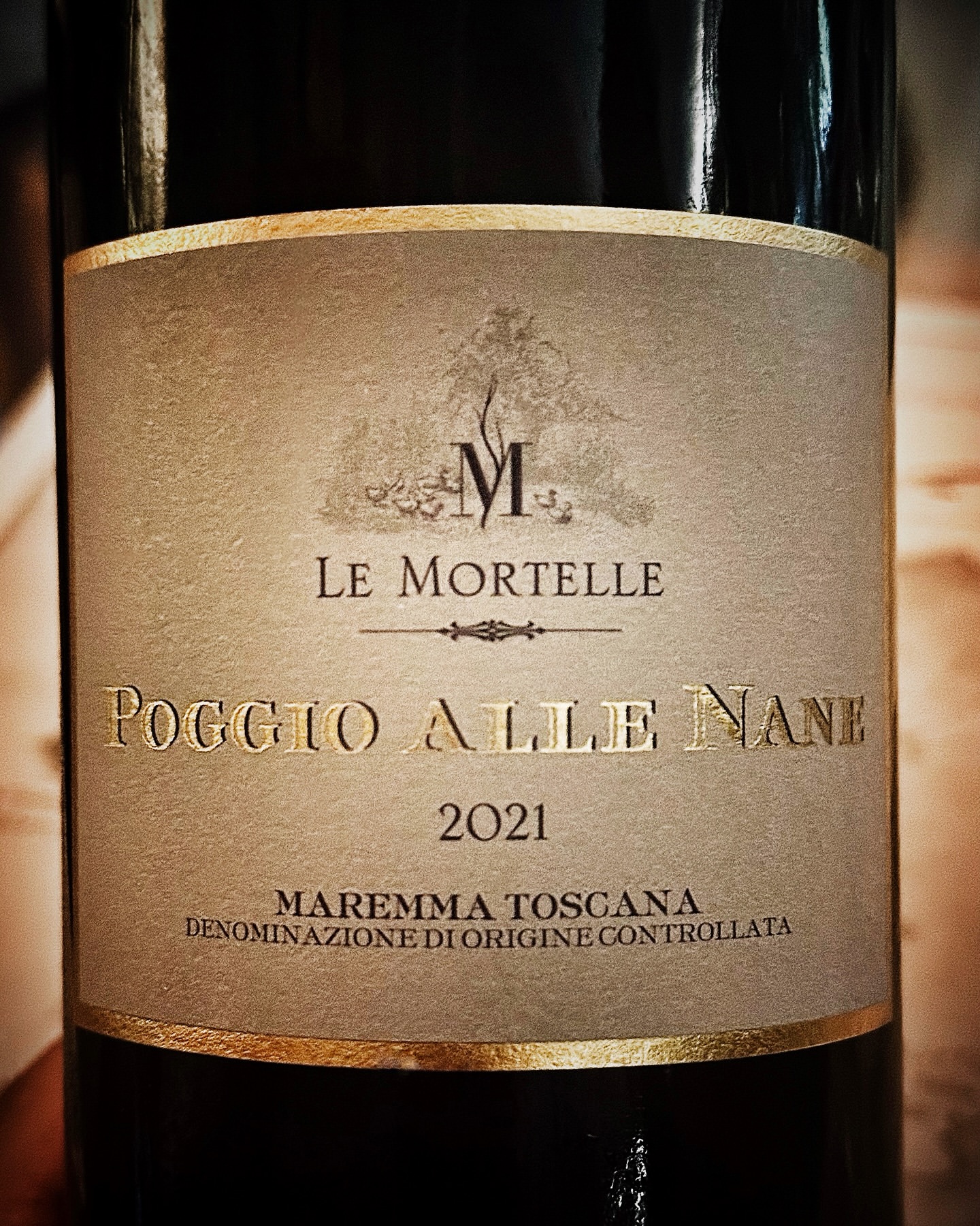 Elegant bottle of Poggio Alle Nane 2021 Maremma Toscana red wine with gold lettering, displayed indoors with a close-up studio shot.