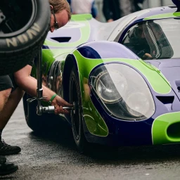 Mechanic using a torque wrench to change a wheel on a purple and green racing car by Michael Haegele