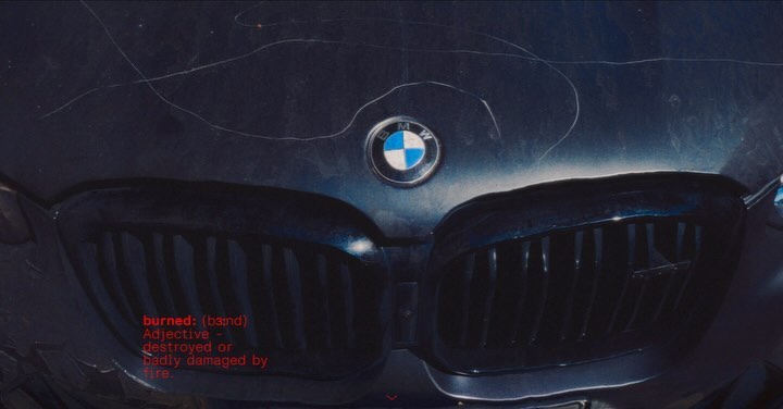 Close-up of a BMW car front grill and hood with damage. The logo is prominently displayed. Dark color tone with visible scratches and dents.