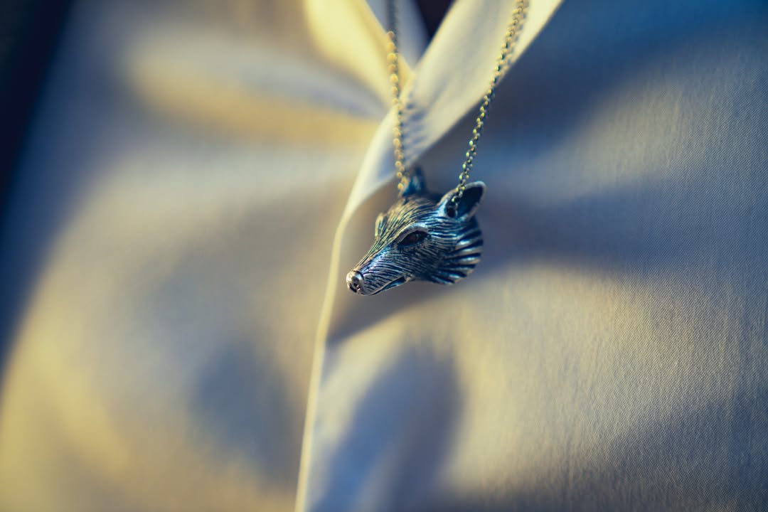 Silver-toned metal fox head pendant necklace on a delicate chain, displayed over a white shirt with soft, diffused studio lighting.