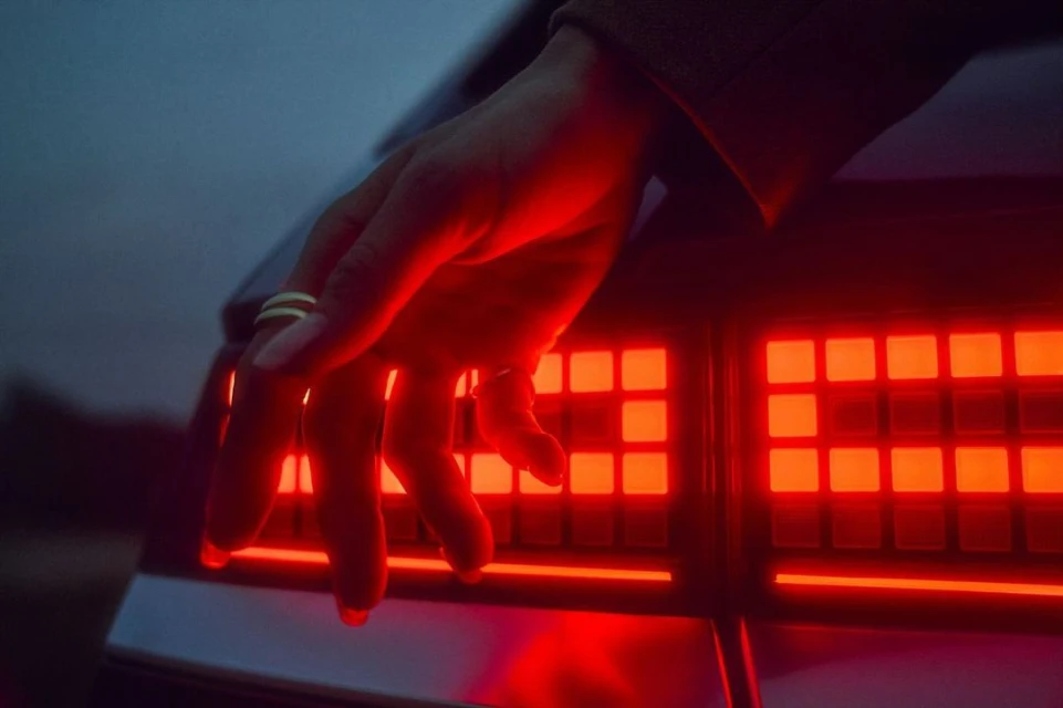 Close-up of a woman's hand resting on the illuminated red taillight of a car, showcasing an automotive detail in a moody ambiance.