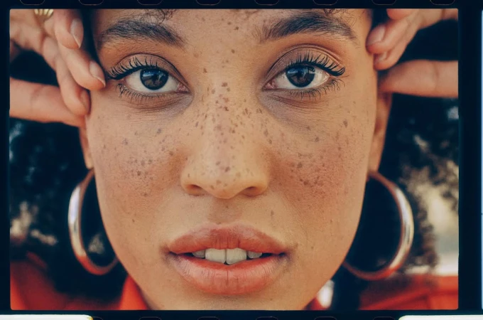 Close-up portrait of a woman with freckles and large silver hoop earrings framed by film sprocket borders